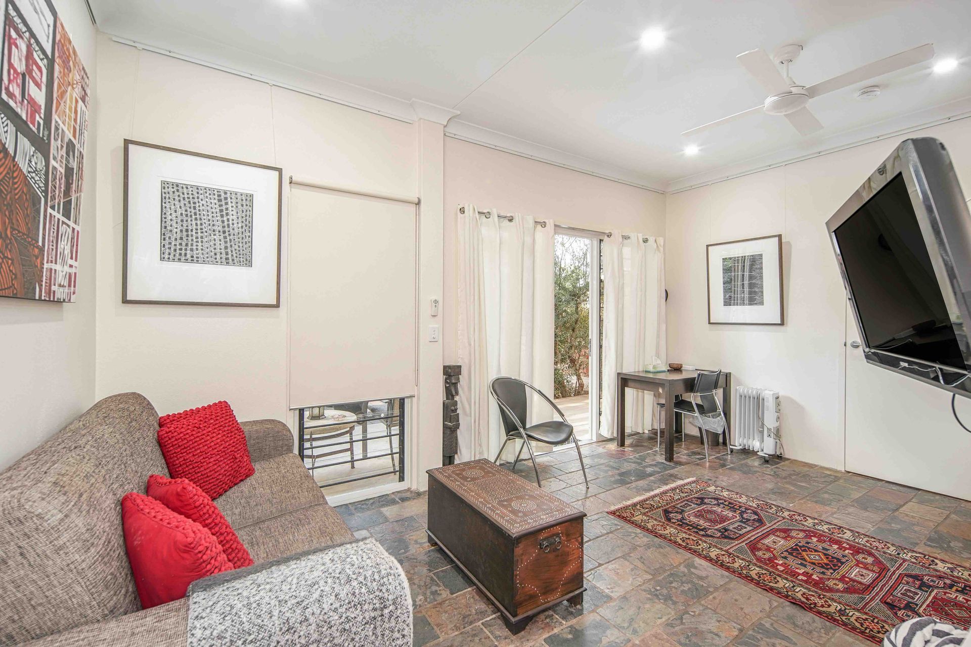 Living room with sofa, red pillows, coffee table, rug, artwork, and a TV.
