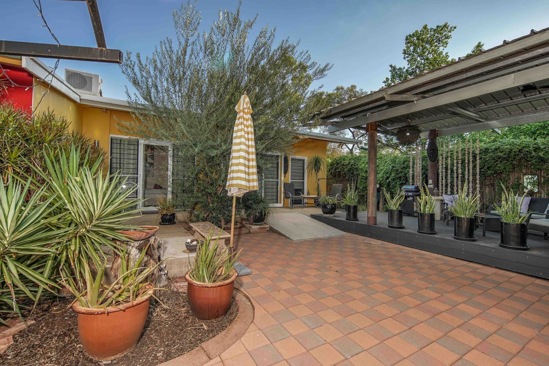 Courtyard with brick patio, potted plants, and covered seating area. Yellow building in background.