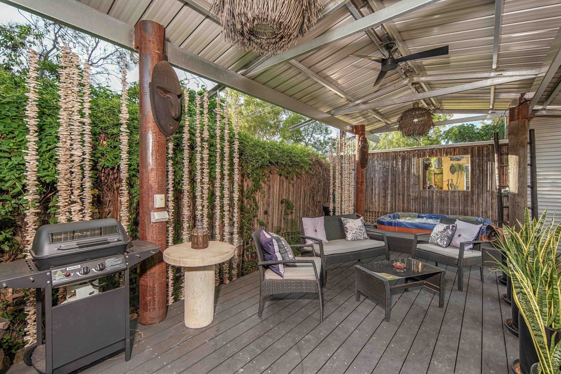 Outdoor patio with grill, seating area, and hot tub under a covered roof.