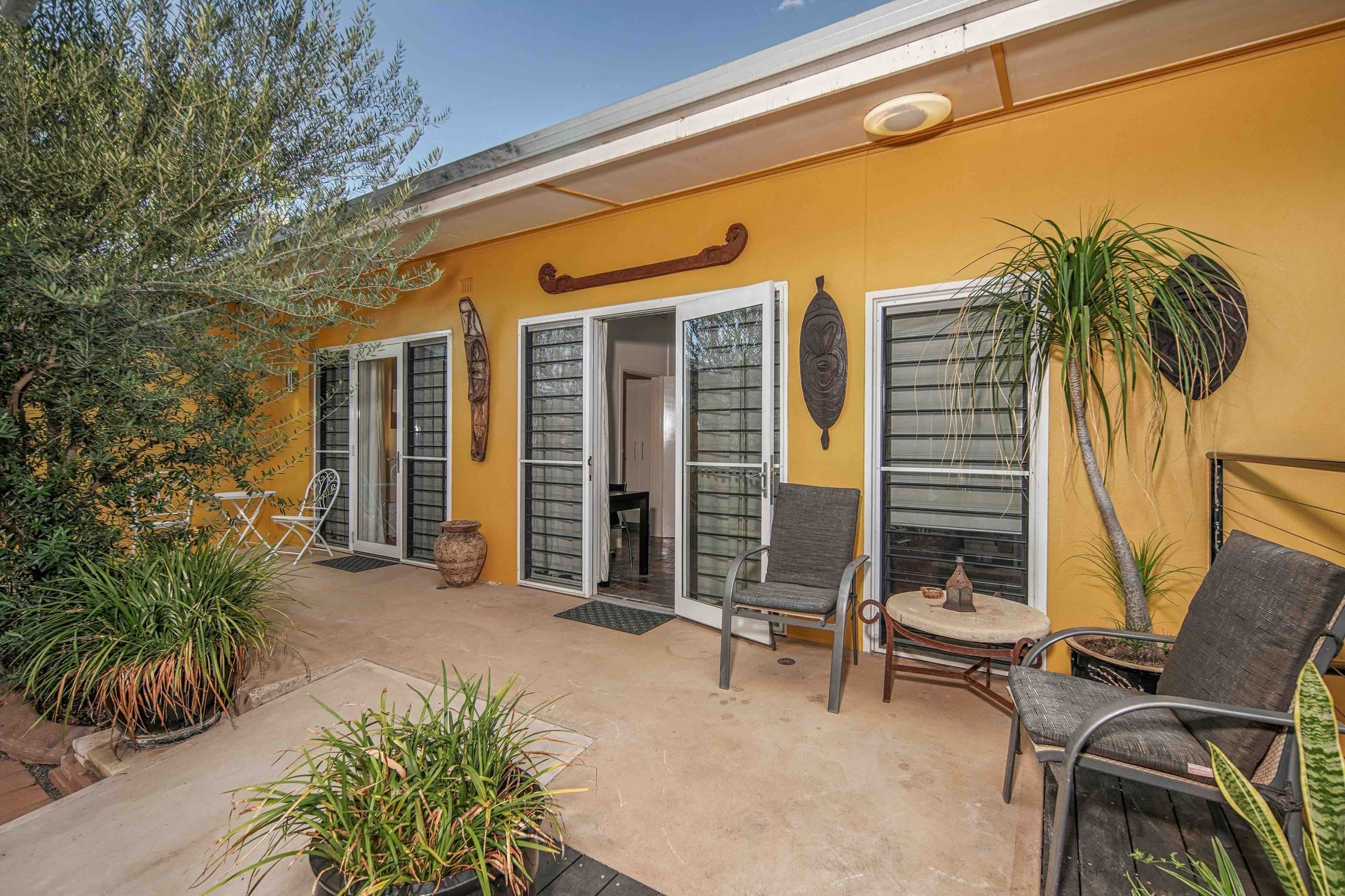 Yellow building with a patio, chairs, potted plants, and glass doors.