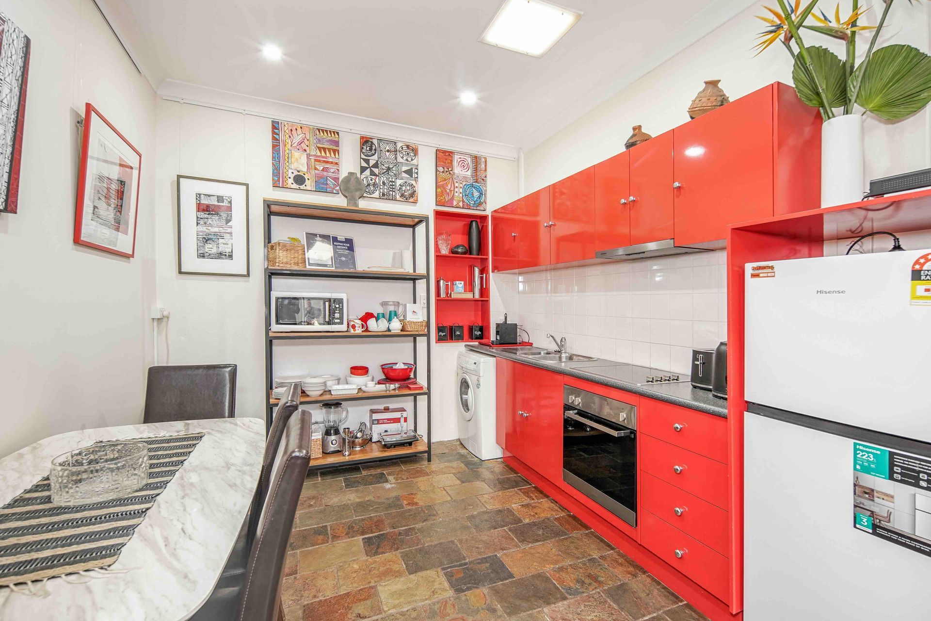 Red kitchen cabinets in a small space, with refrigerator, oven, microwave and dining area.