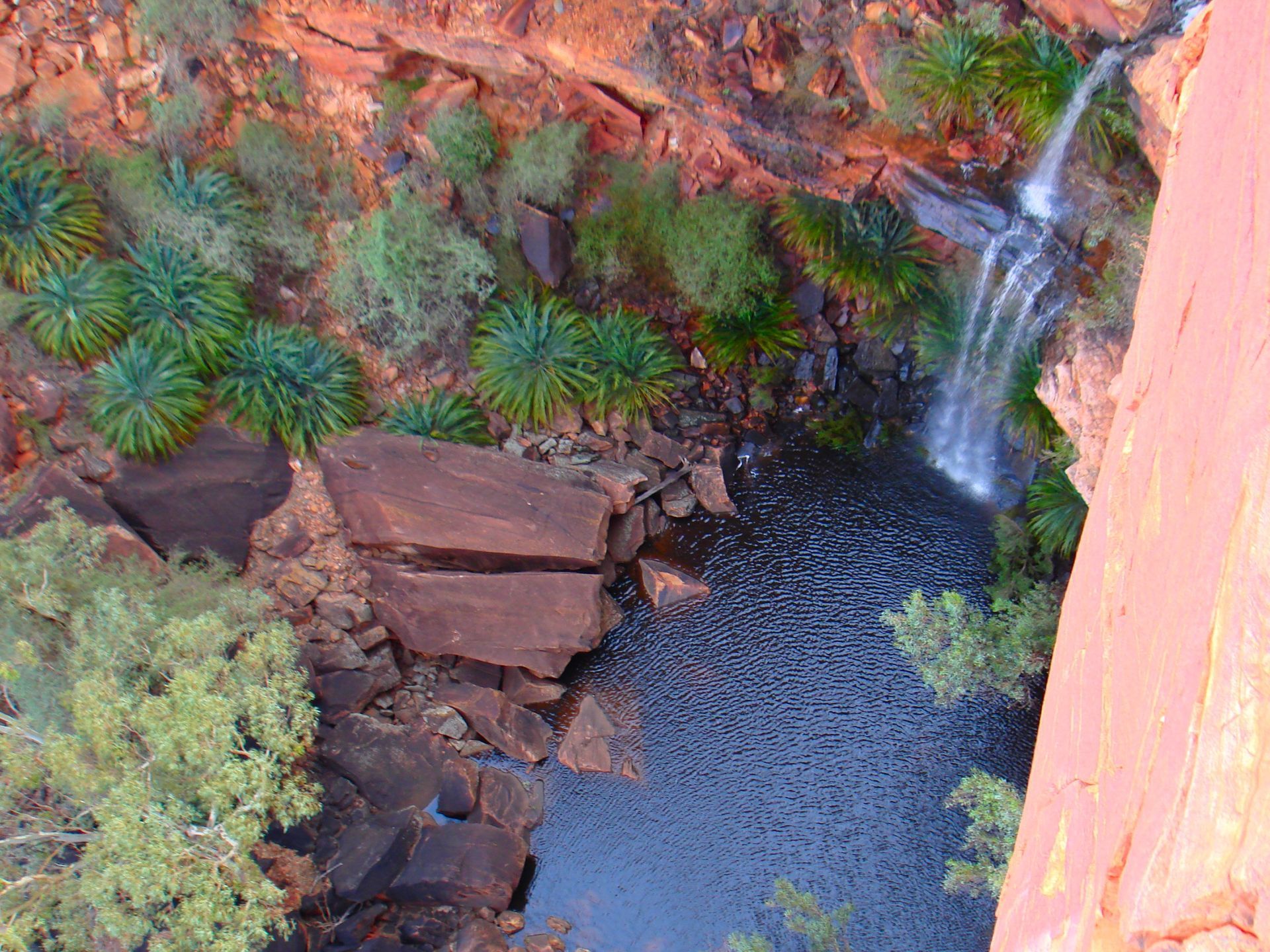 Waterfall cascading into a dark pool at the bottom of a red rock canyon.