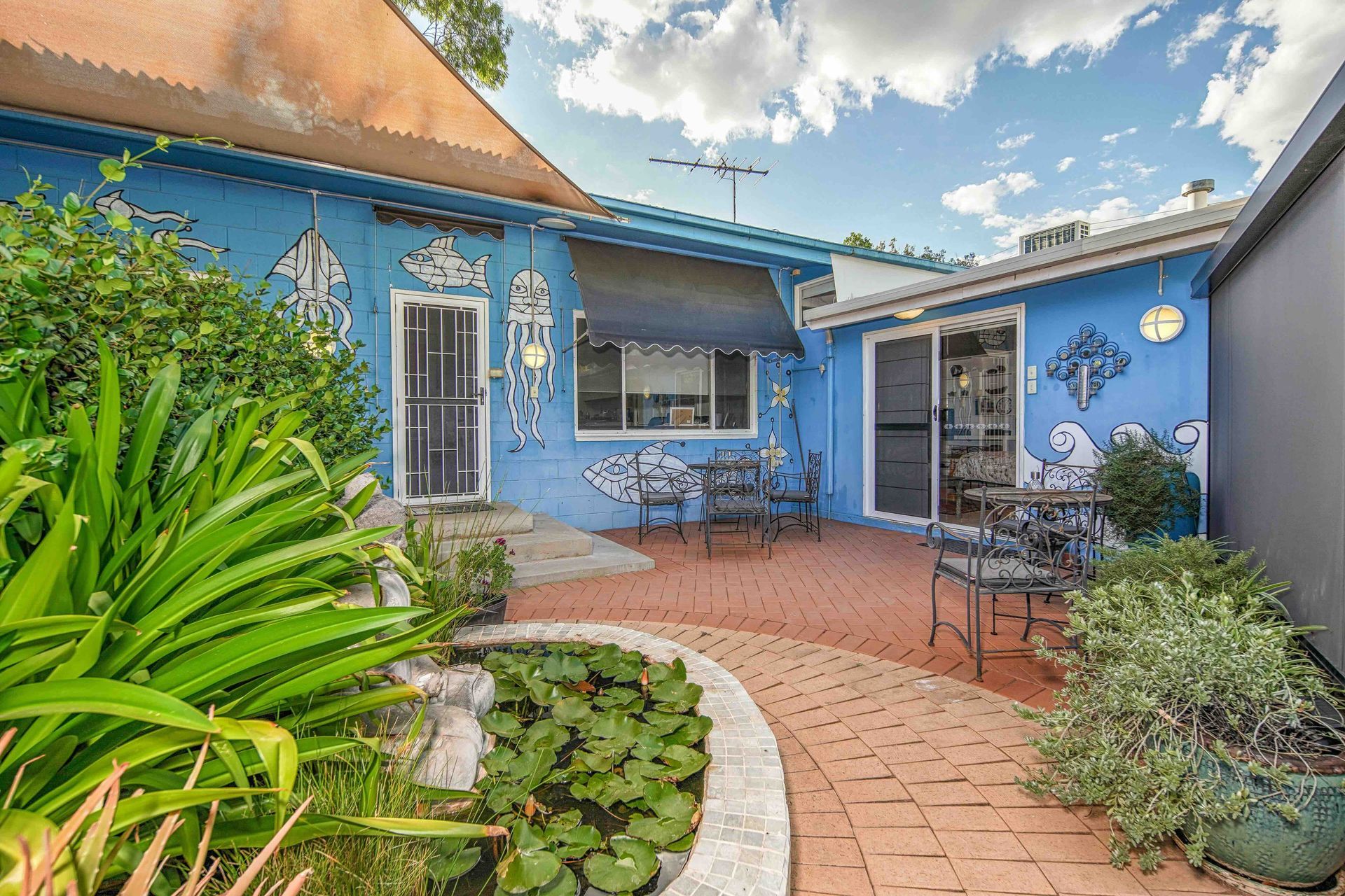 Blue house with patio, small pond, and decorative elements. Sunny day, exterior shot.