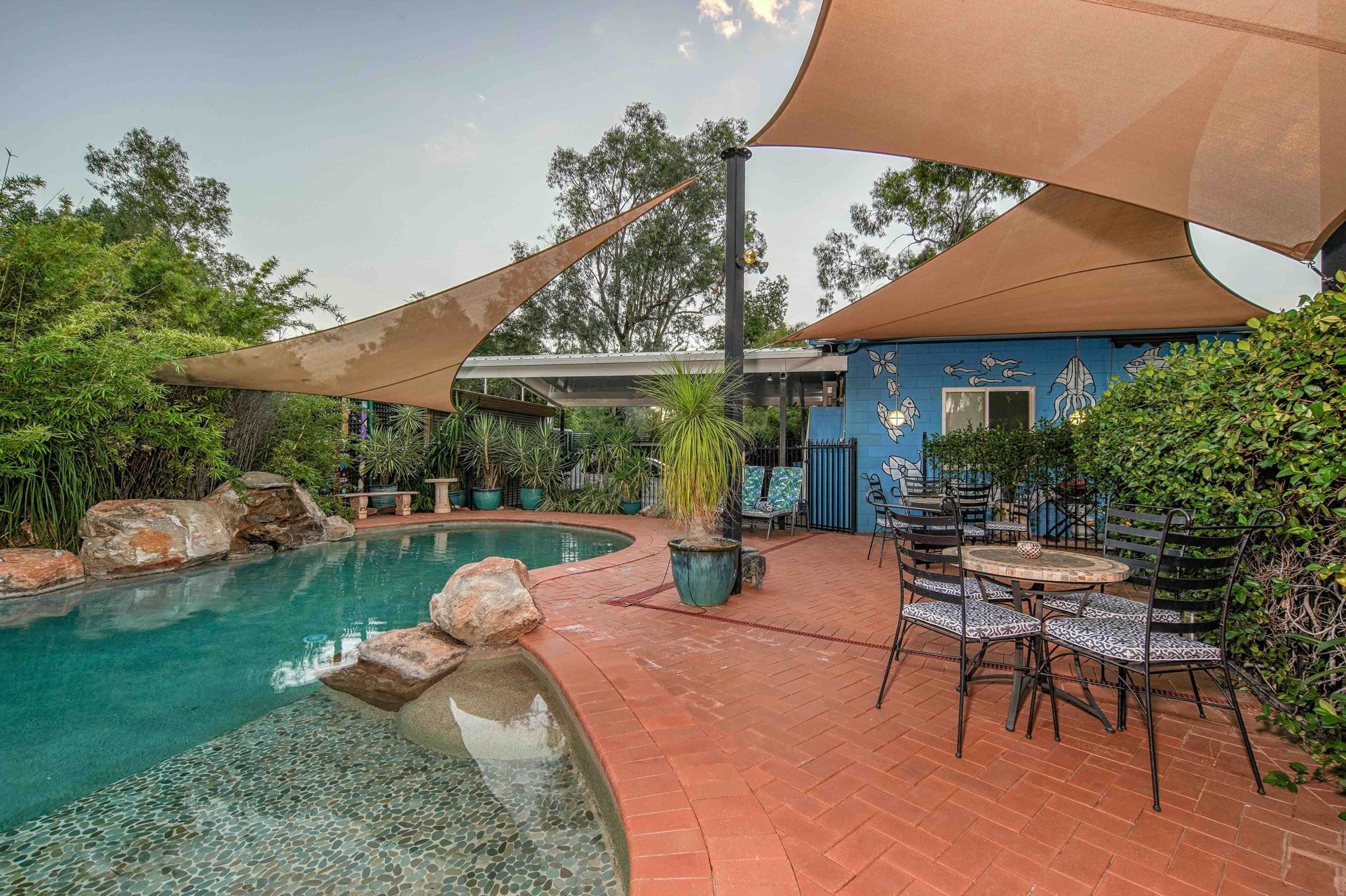 Pool area with sun shades, patio furniture, and blue building.