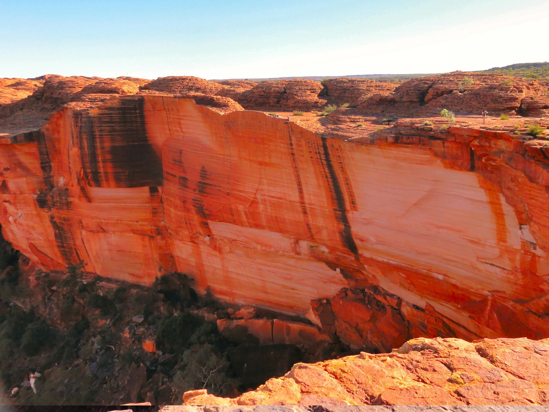 Red and brown sandstone cliff face with layered rock formations under a blue sky.