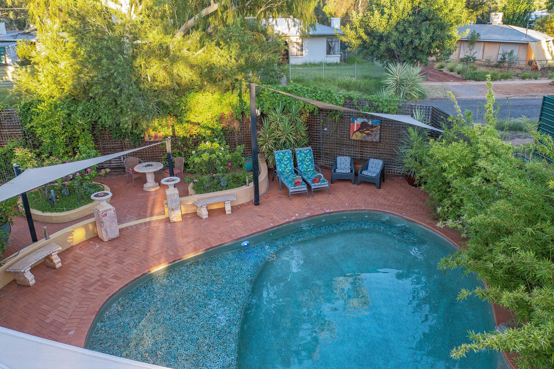 Pool and patio with lounge chairs, shade sails, and surrounding greenery.