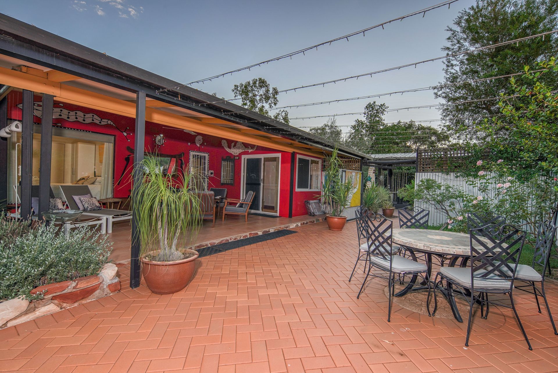 Red brick patio with outdoor furniture and red building with a covered porch; string lights overhead.