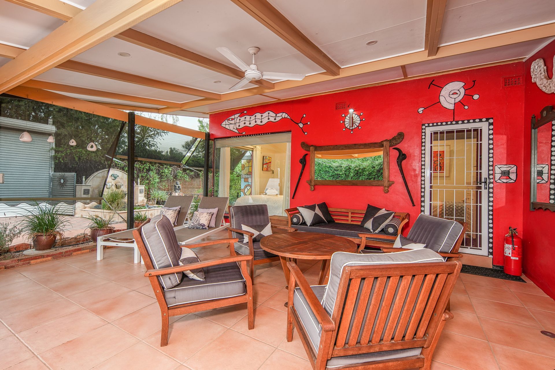 Patio seating area with red wall, wooden furniture, and garden view.
