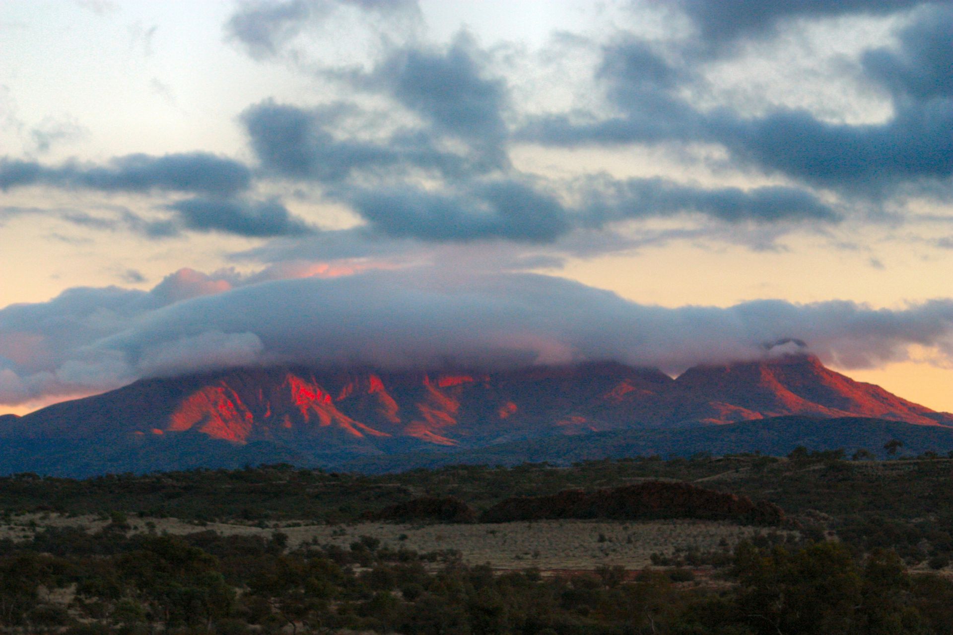 Mountain at sunset, clouds partially obscuring its peak; reddish hues illuminate its slopes.