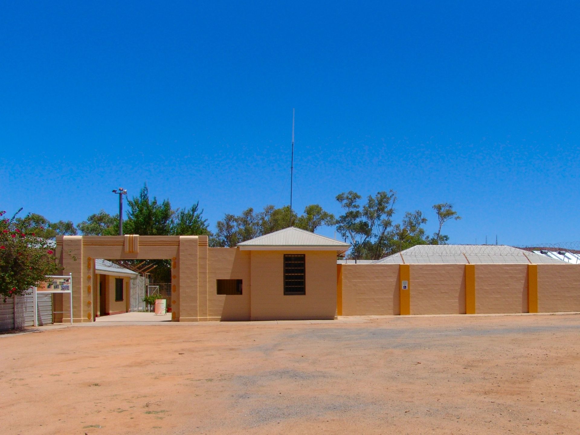 Beige brick building with gated entrance and tall antenna under a clear blue sky.