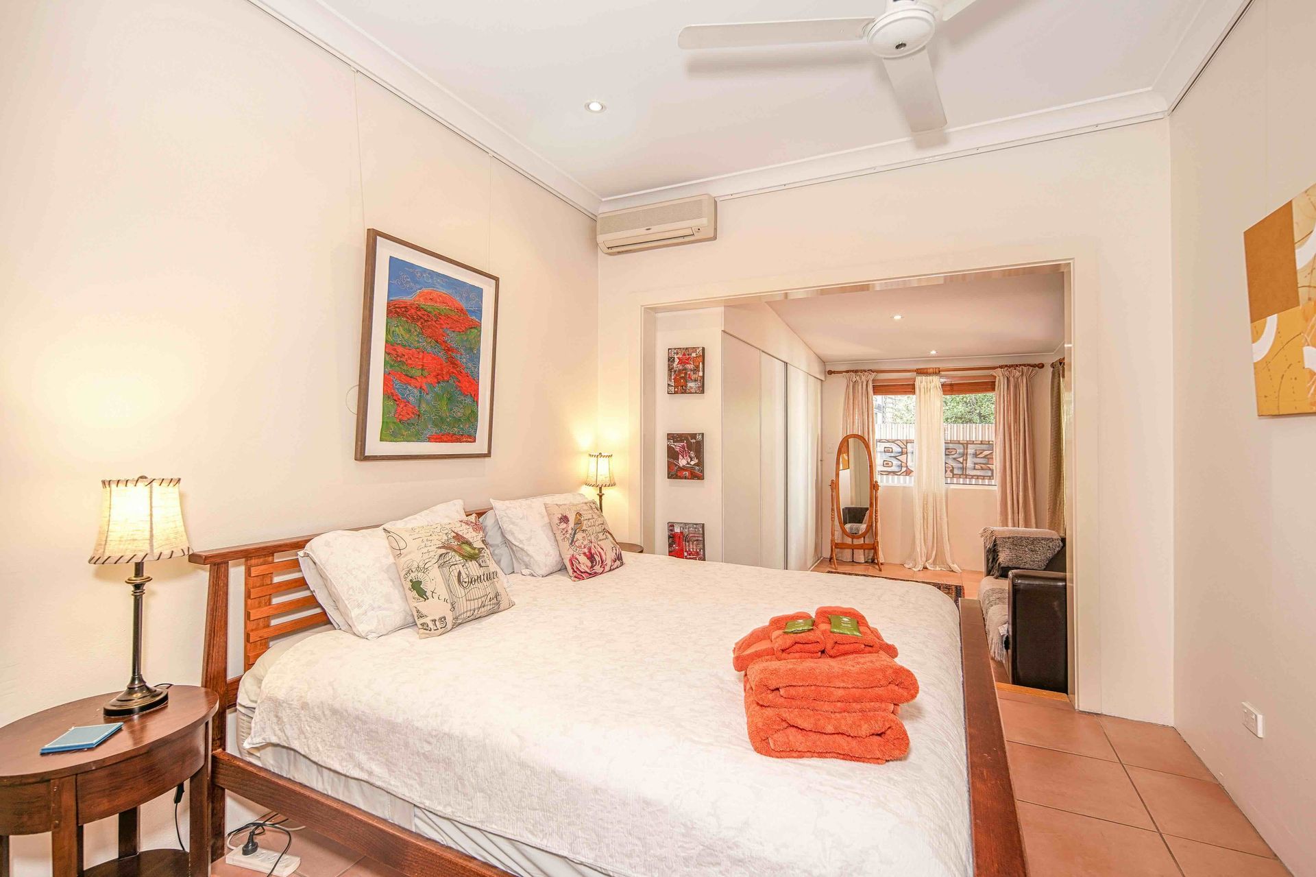 Bedroom with a large bed, side table, artwork, and doorway leading to another room.