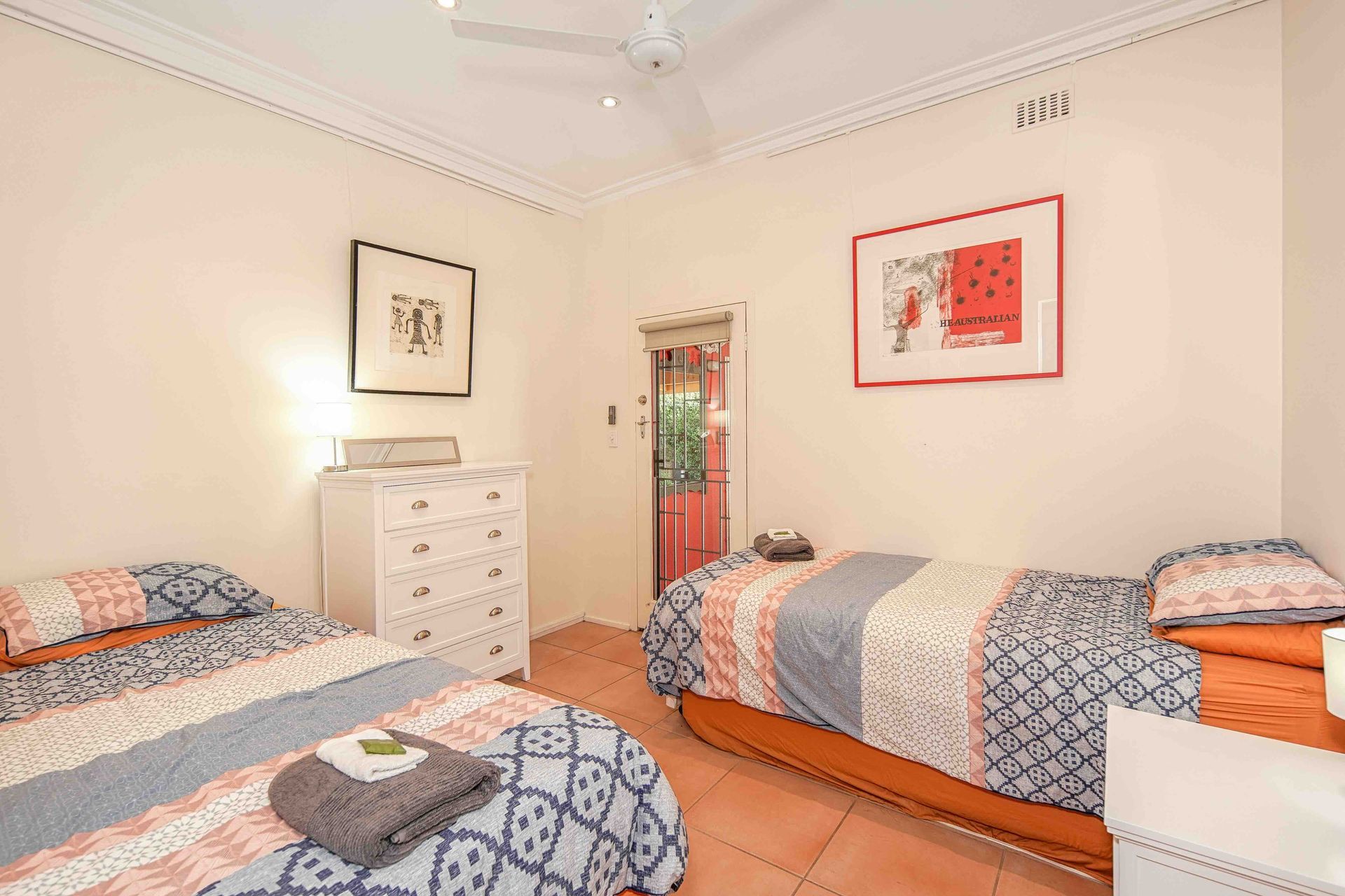 Bedroom with two twin beds, white dresser, artwork, and doorway.