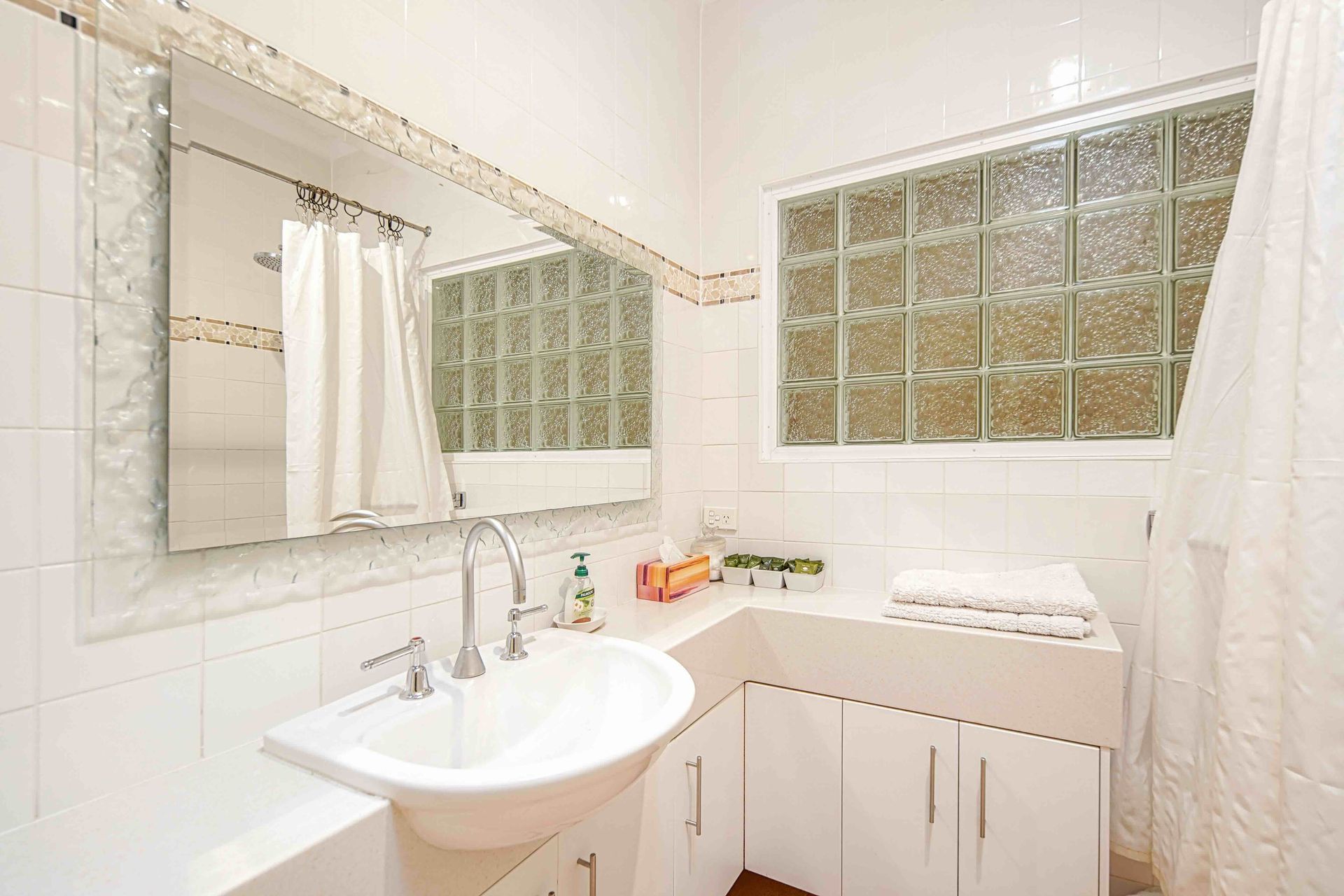 White bathroom with sink, mirror, glass block window, and shower curtain.