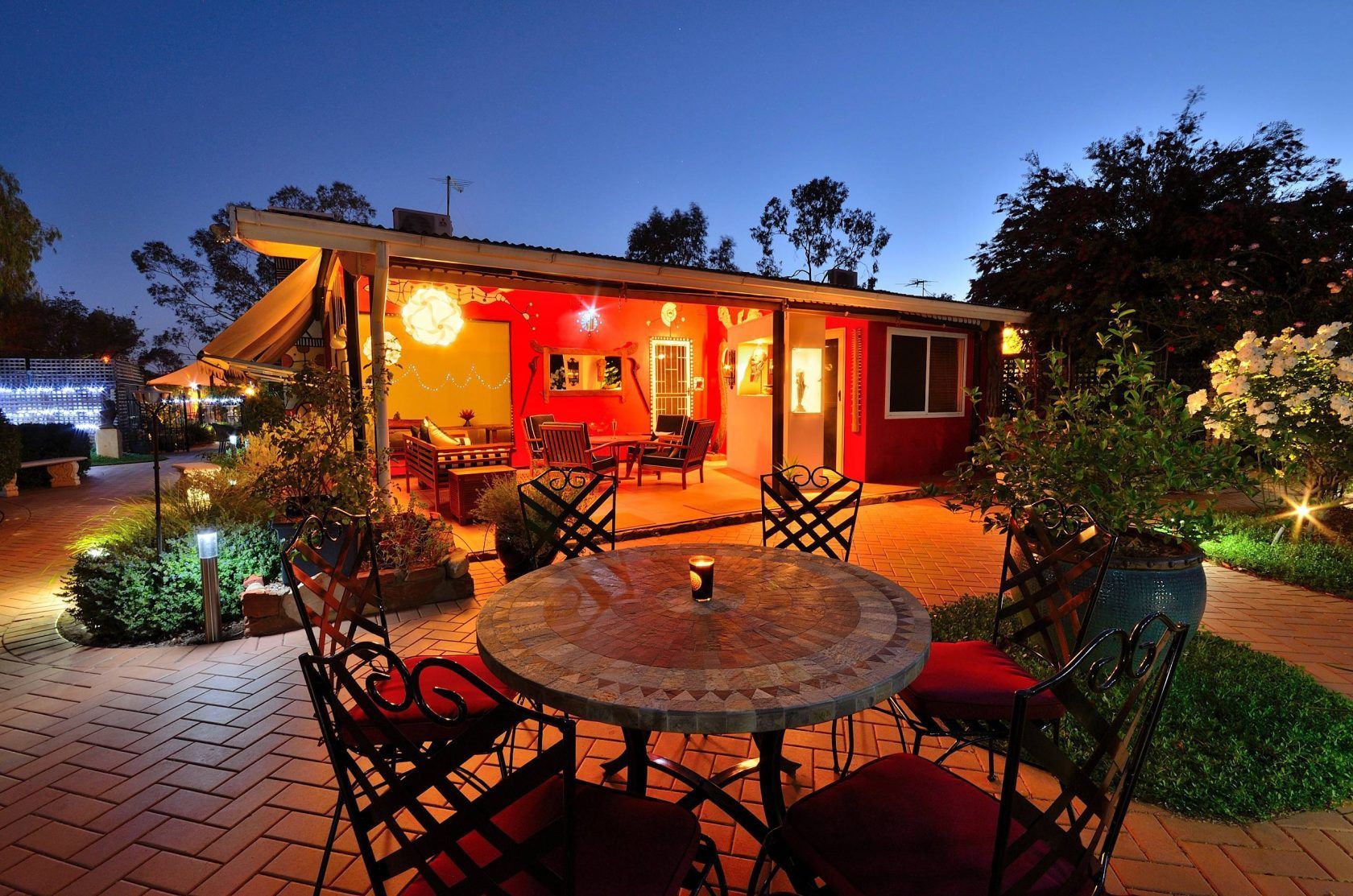 Outdoor patio with mosaic table and chairs, illuminated red building, night.