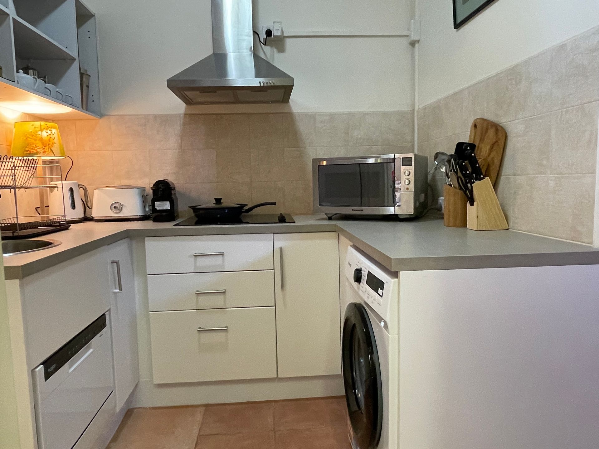 A small, white, U-shaped kitchen with appliances, including a washing machine and microwave.