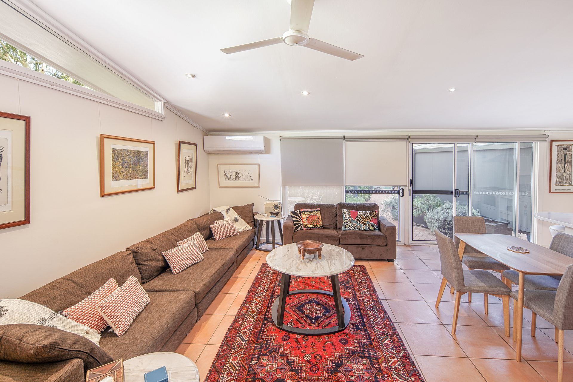 Living room with long brown sofa, dining table, and rug.