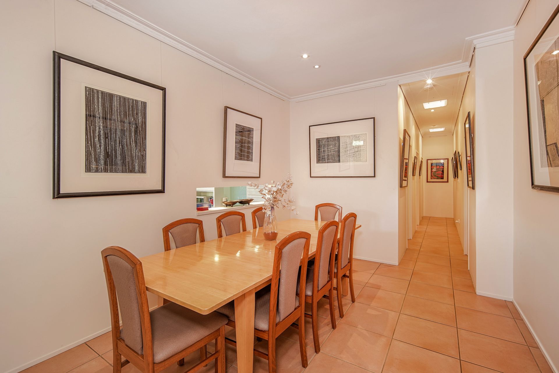 Dining room with table and chairs, artwork on walls, and hallway leading to other rooms.