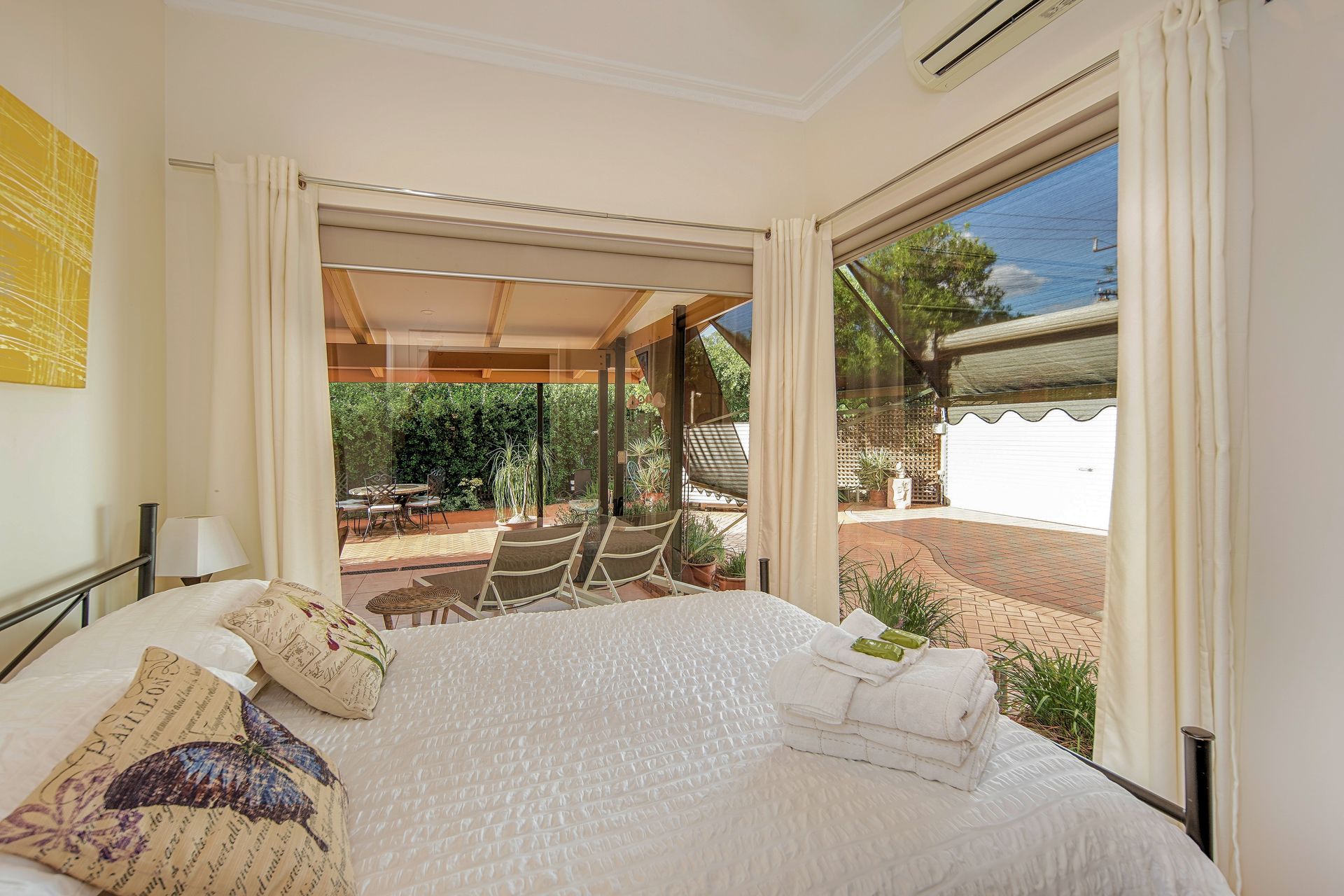 Bedroom with bed, open doors to patio with outdoor furniture, bright light.