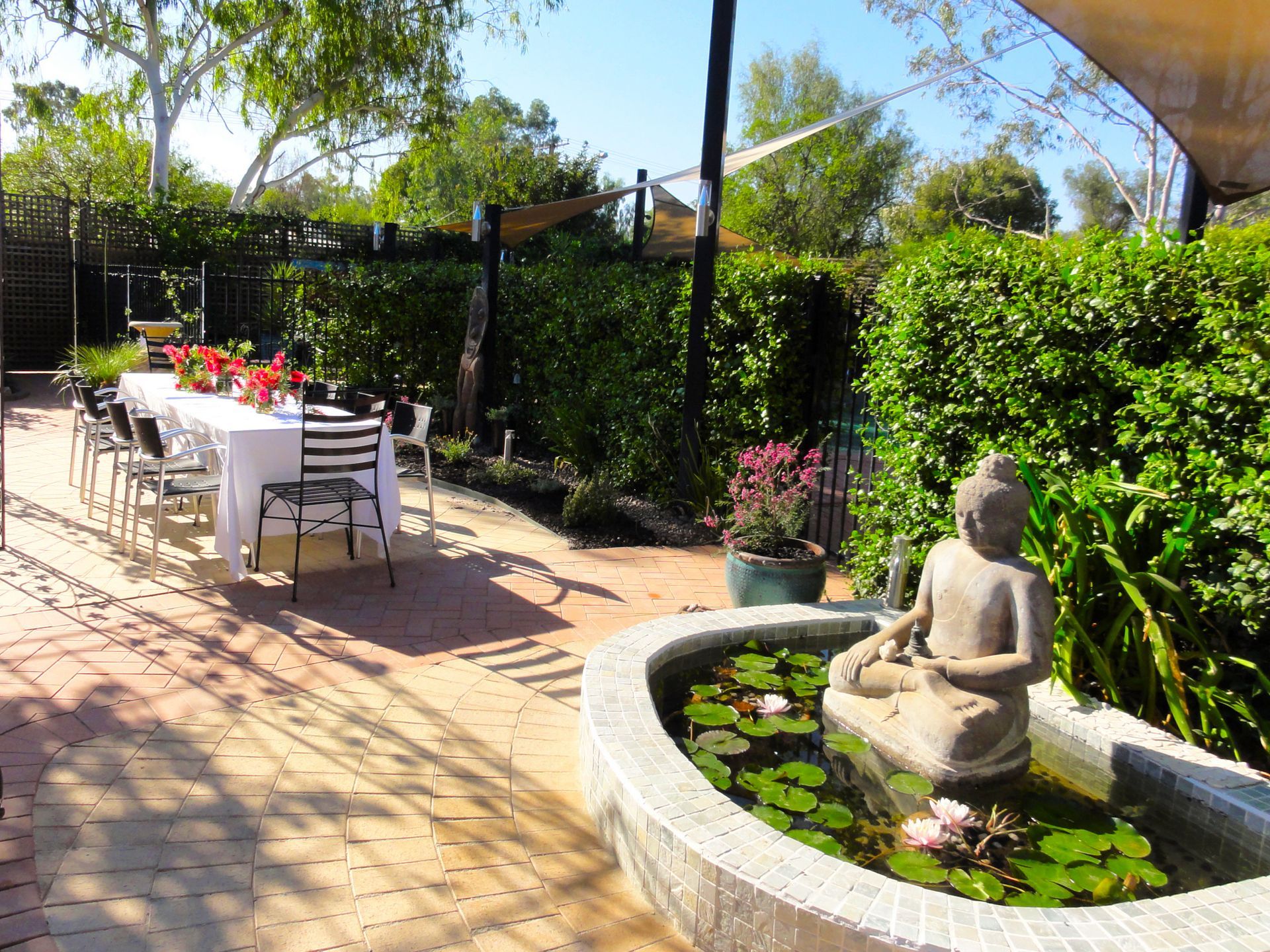 Outdoor patio with dining table, Buddha statue in a pond, and lush greenery.