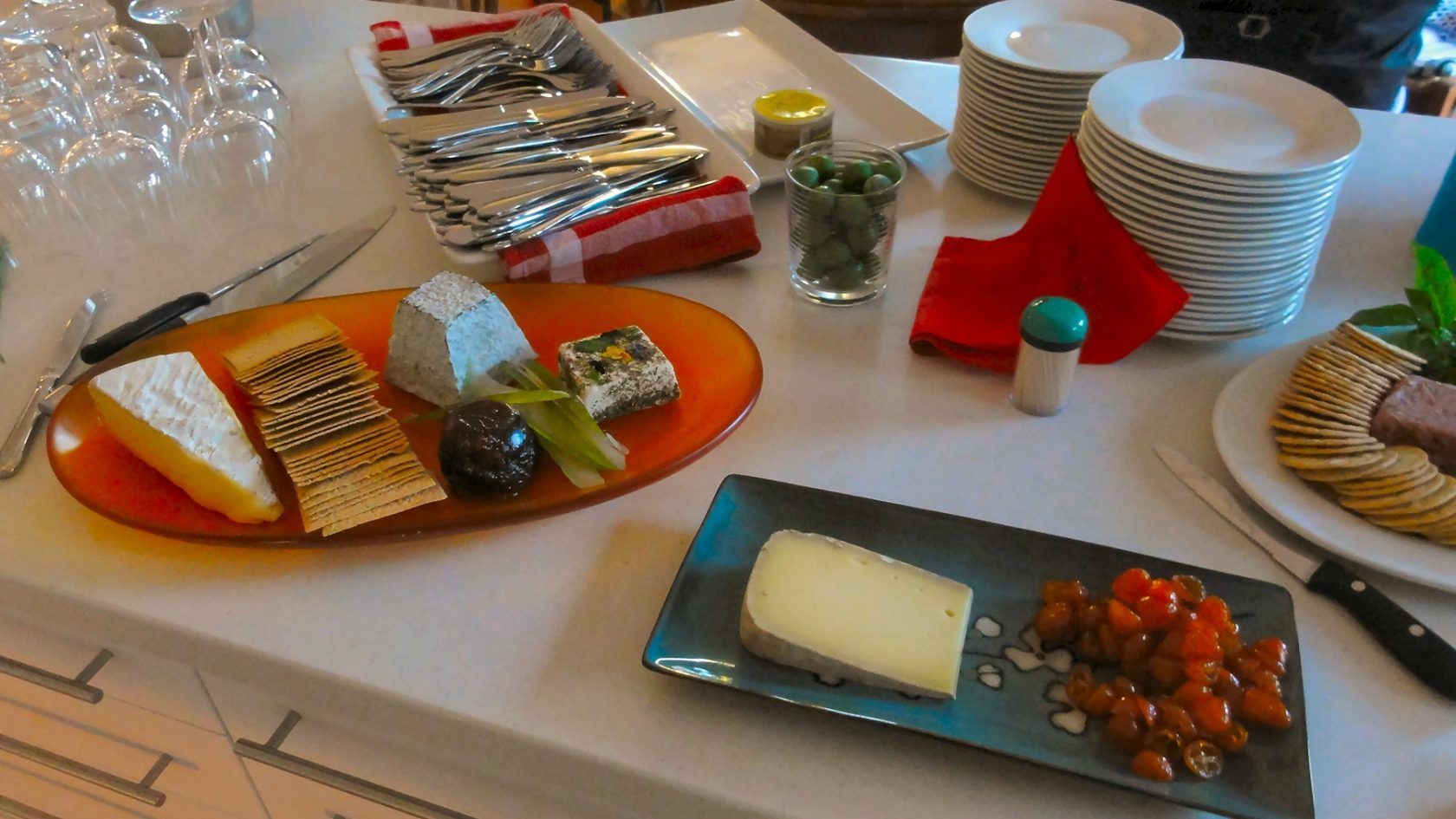 Cheese and cracker plates with various cheeses, olives, and condiments, set on a table.