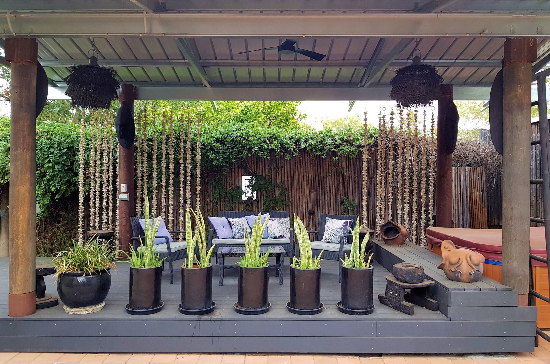 Outdoor lounge area with potted plants, bamboo screen, seating, and decorative hanging spheres.