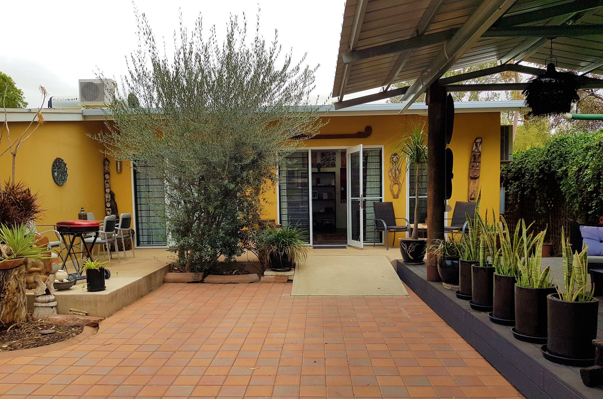 Yellow house with red brick patio, outdoor seating, plants, and a covered patio area.