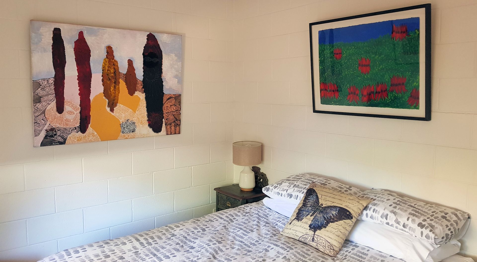 Bedroom with artwork on white block walls, bed, nightstand, and lamp.