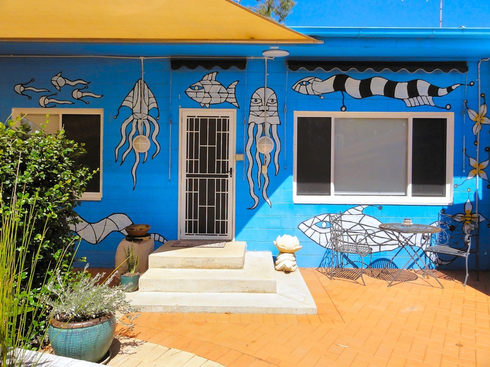 Blue building with sea creature murals, door, windows, and outdoor seating.