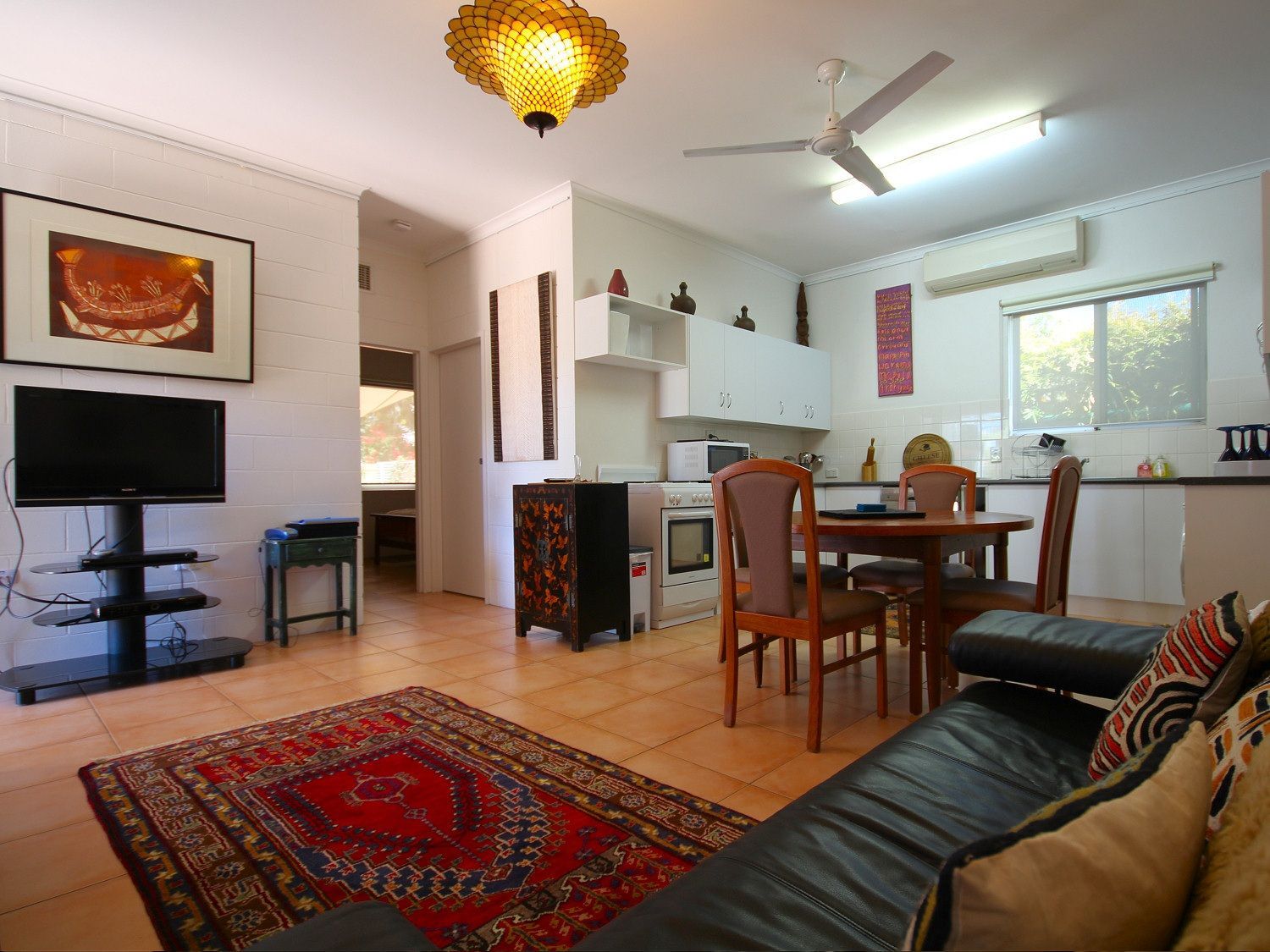 Living room with a black leather couch, red rug, TV, dining table, and kitchen in the background.