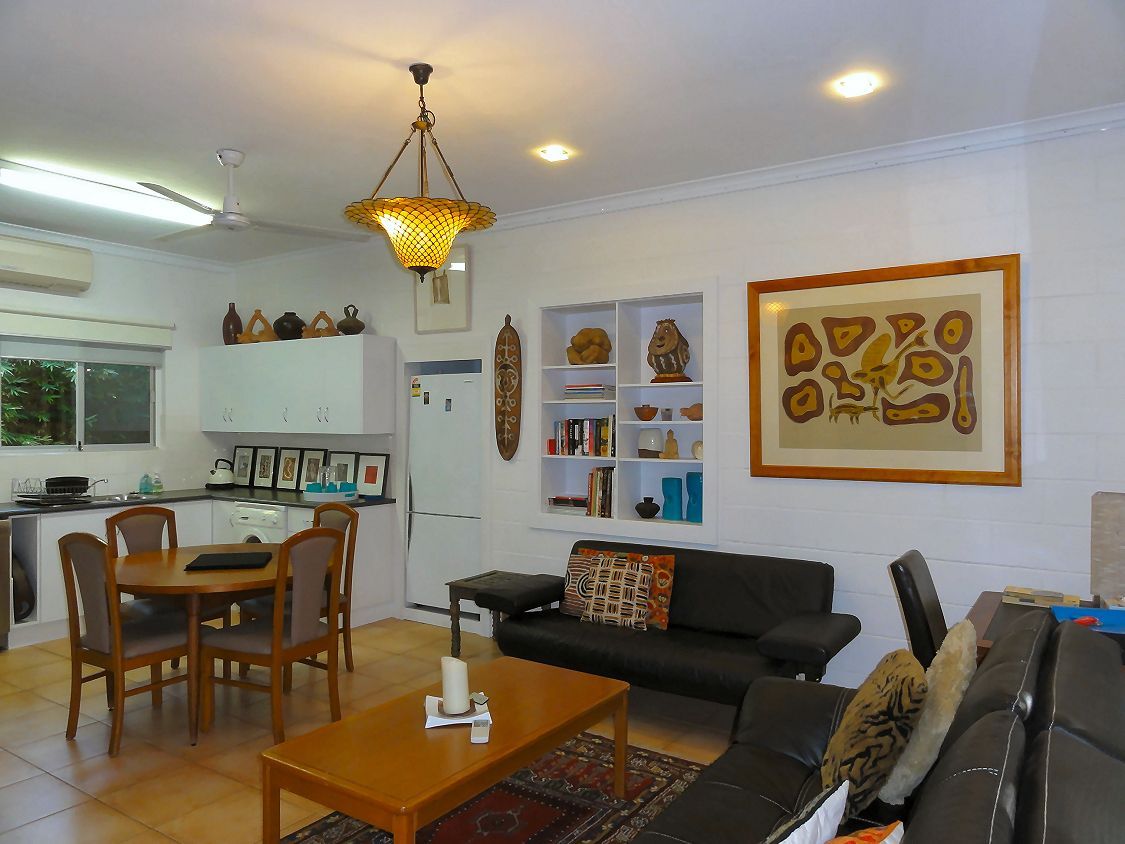 Living room with kitchen. Dark leather sofas, wooden table, round dining table, artwork, and various decorative items.
