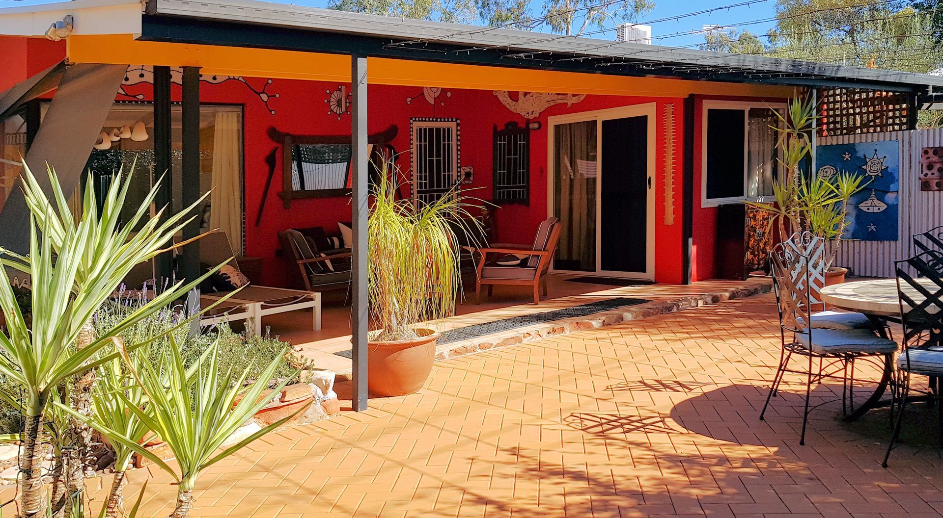Red stucco building with terracotta patio, outdoor furniture, and potted plants under a yellow awning.