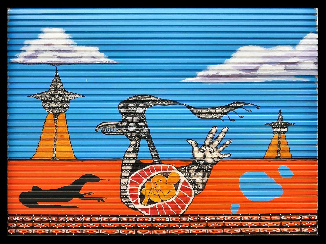 Abstract art with alien landscape: orange ground, blue sky, two towers, a hand, bird-like figure.