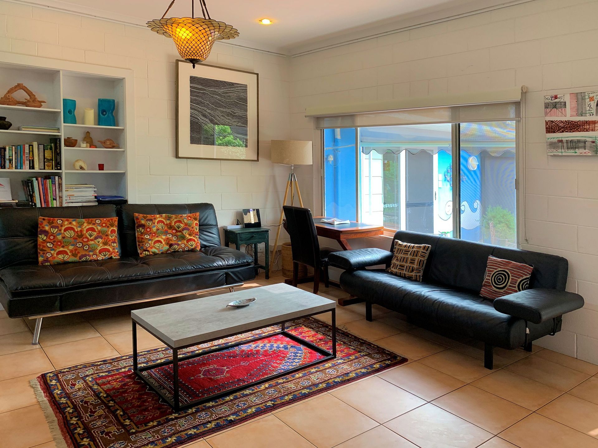 Living room with black sofas, a coffee table, and a bookshelf. A rug and artwork complete the space.