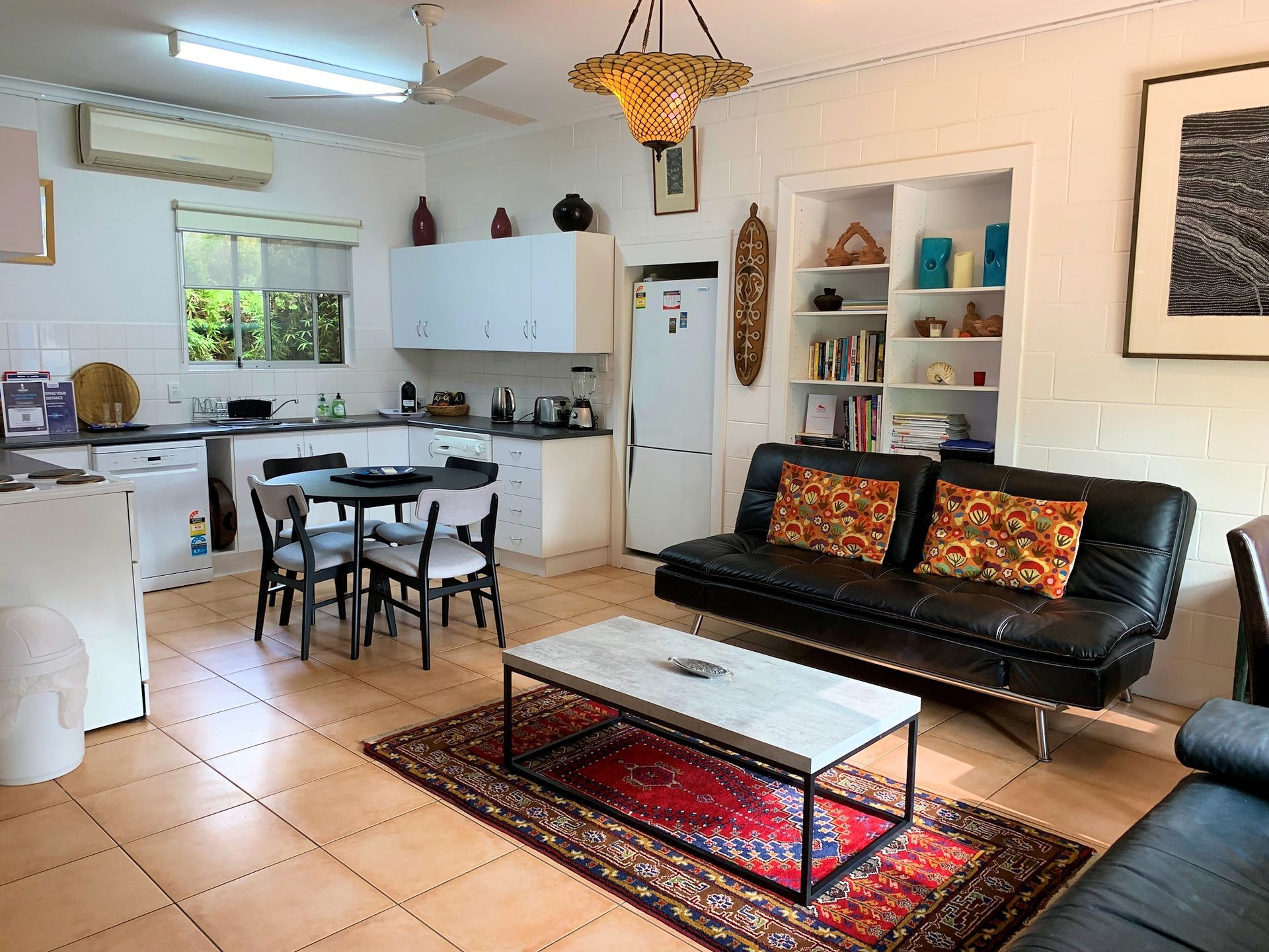 Interior of a living space with a kitchen. Black sofa, coffee table, rug, and shelves.