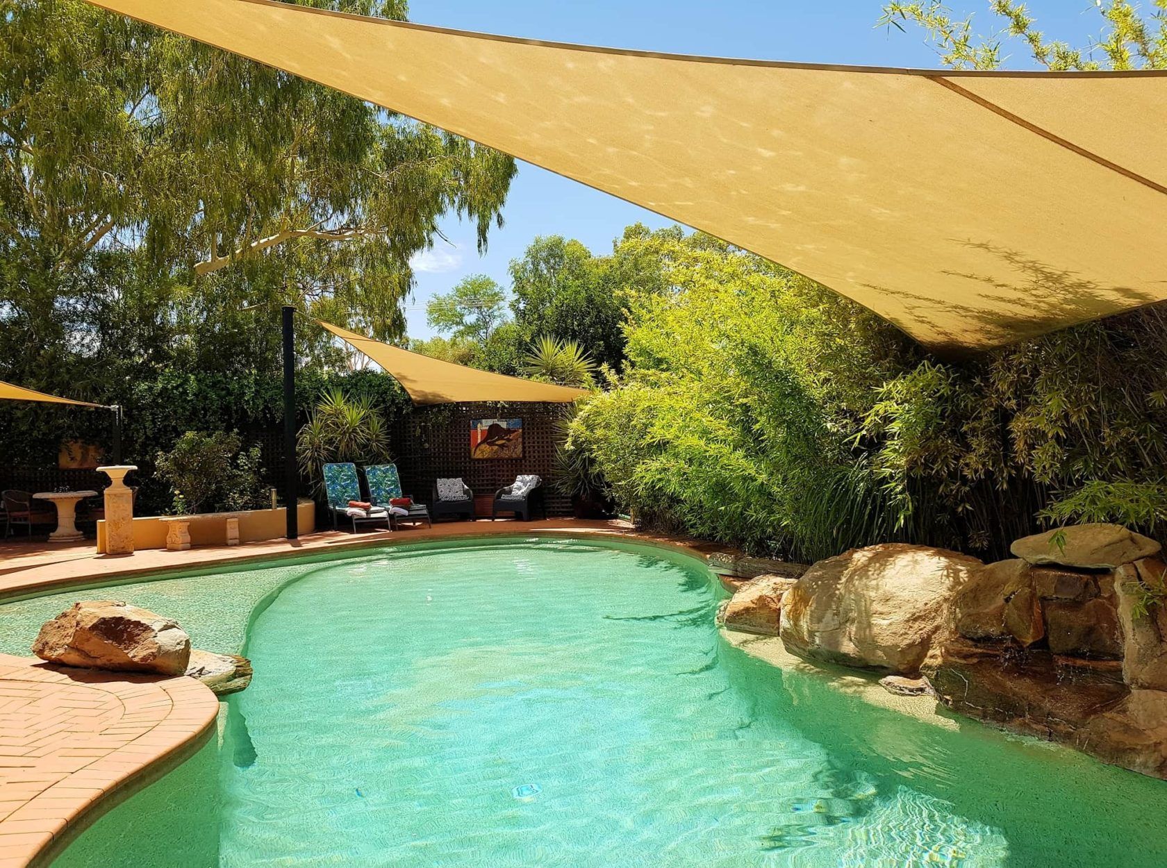 Swimming pool with shade sails, lounge chairs, and lush landscaping.