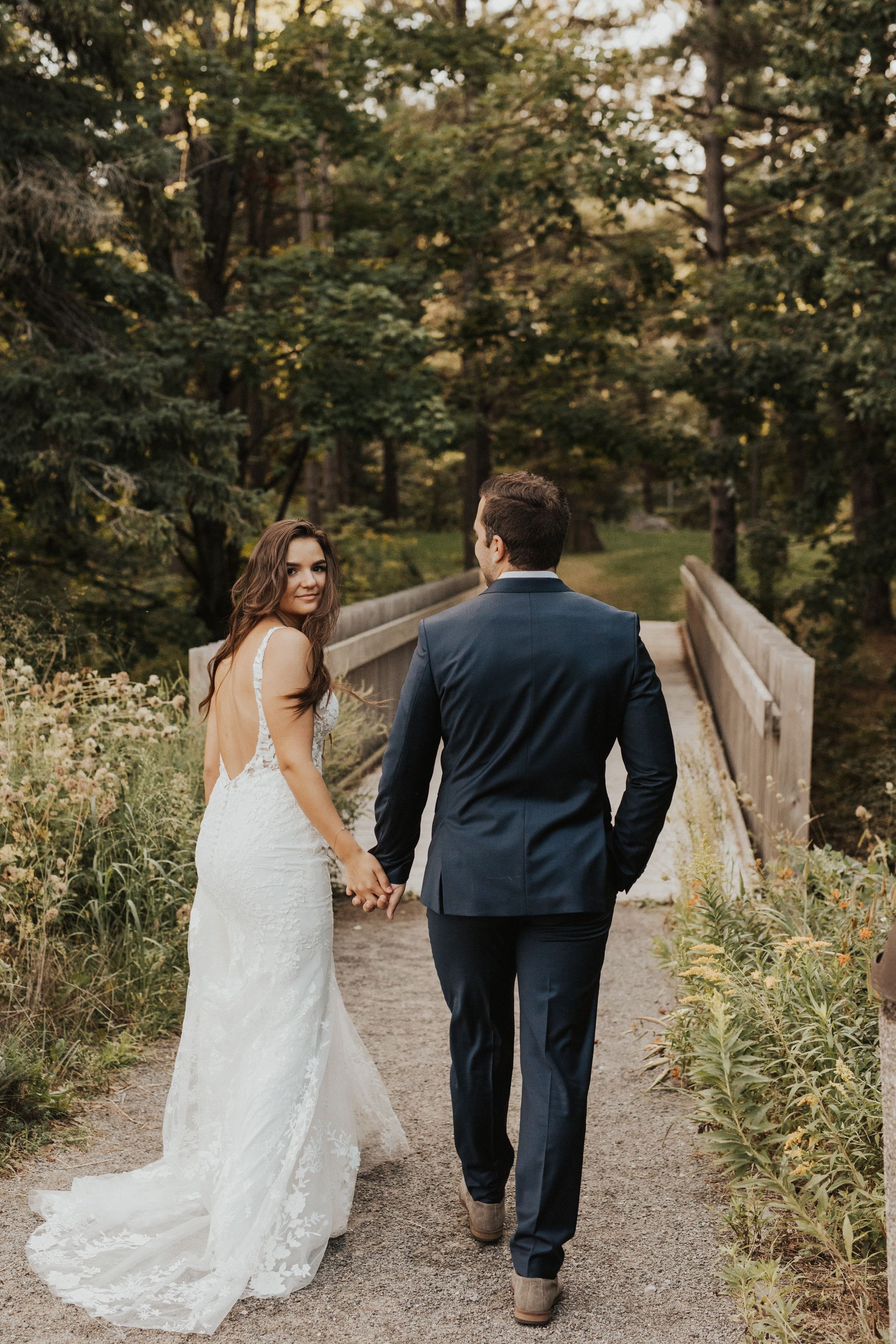Bride and groom holding hands on a wooden bridge in a wooded garden path