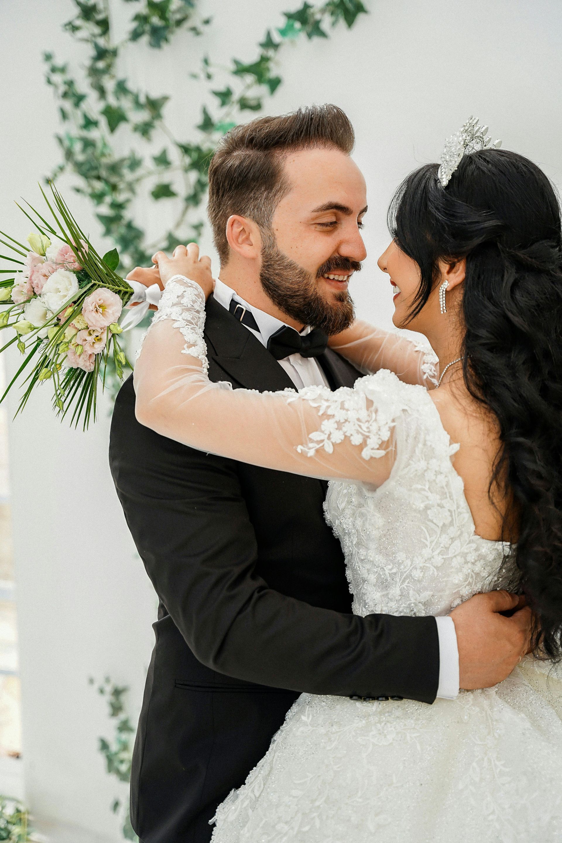 Couple embracing at their wedding, with the bride in a white lace dress and the groom in a black suit