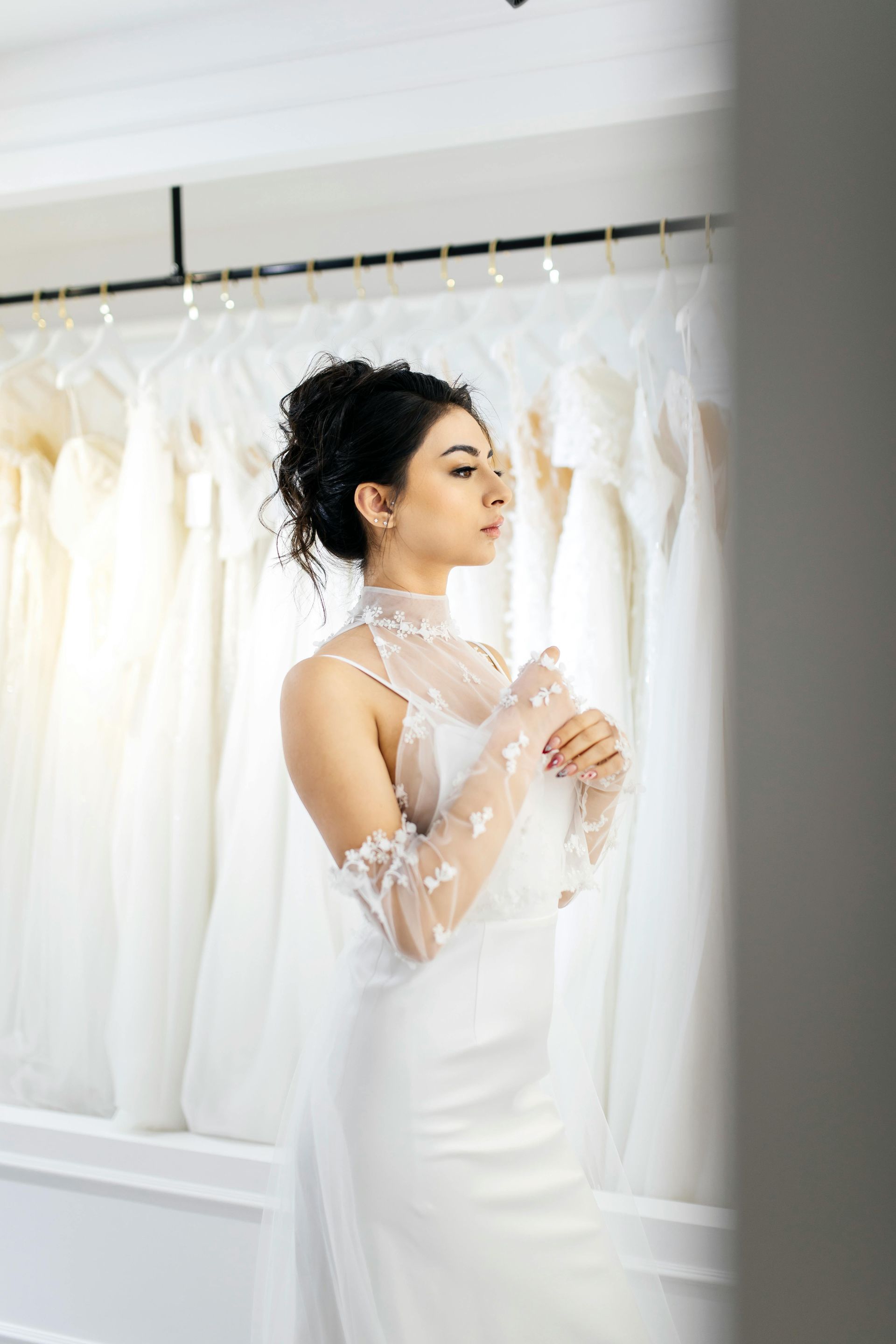 Woman in a white dress standing in a bridal boutique beside rows of hanging white gowns