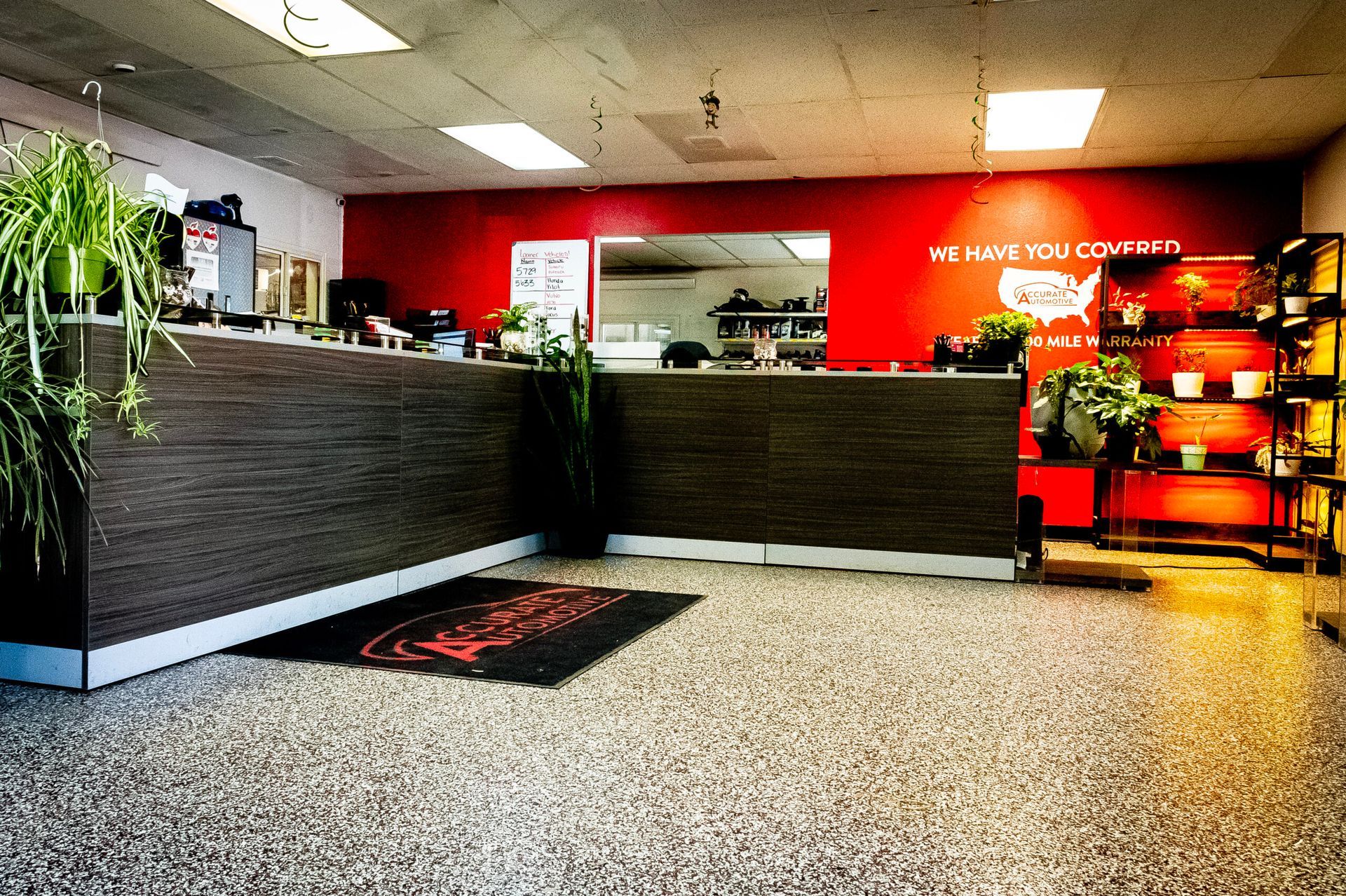 Modern office lobby with a front desk, potted plants, red wall, and seating area | Accurate Automotive Northglenn