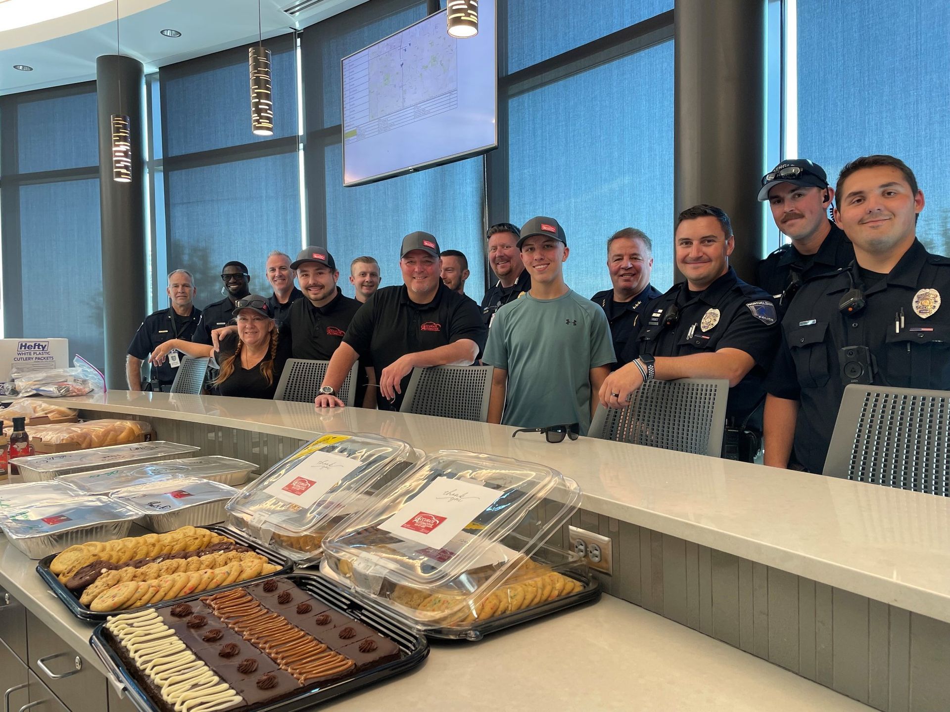 Group of people, including police officers, standing behind a long counter of baked goods in a bright lobby | Accurate Automotive Northglenn