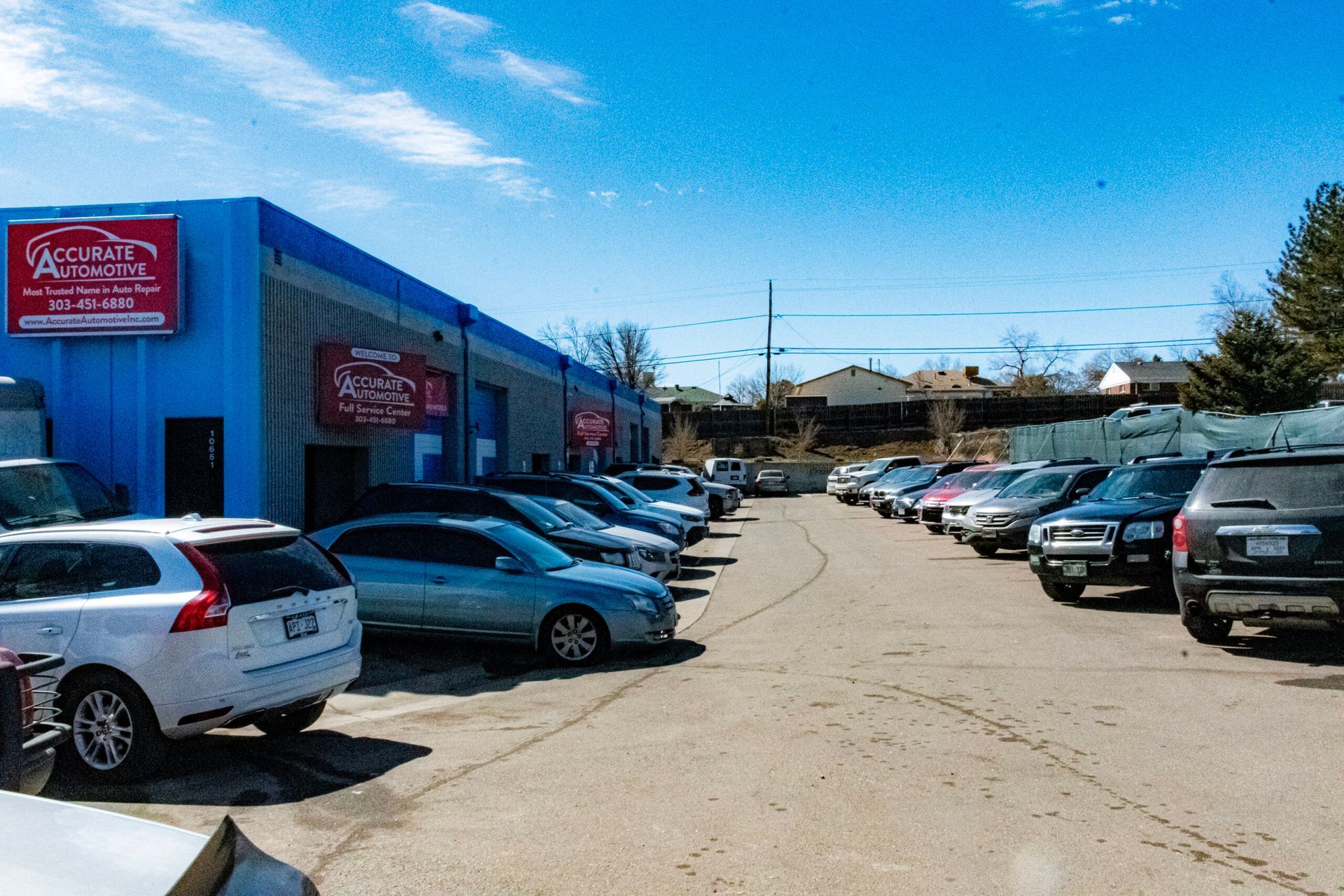 Parking lot beside a blue commercial building with rows of parked cars on both sides. | Accurate Automotive Northglenn