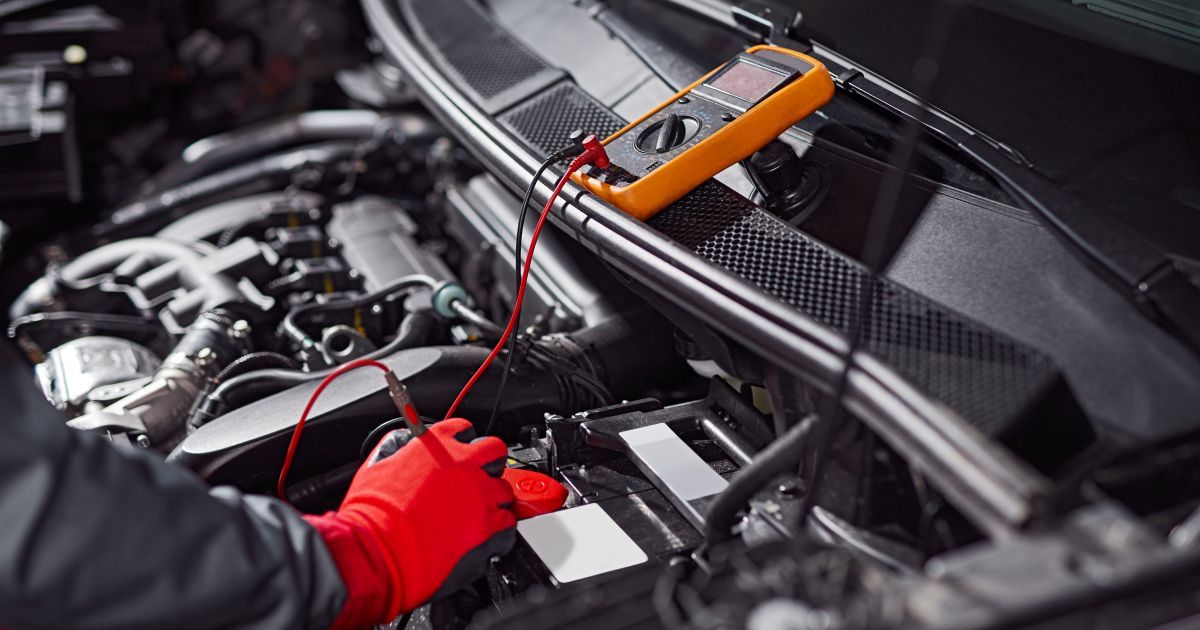 Mechanic testing car engine with a multimeter and red gloves under the hood | Accurate Automotive Northglenn