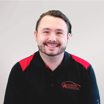 Smiling employee in a black and red Accurate Automation shirt against a light gray background | Accurate Automotive Northglenn