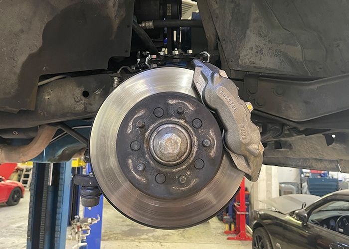 Car brake rotor and caliper exposed in a shop lift, with wheel removed | Accurate Automotive Northglenn
