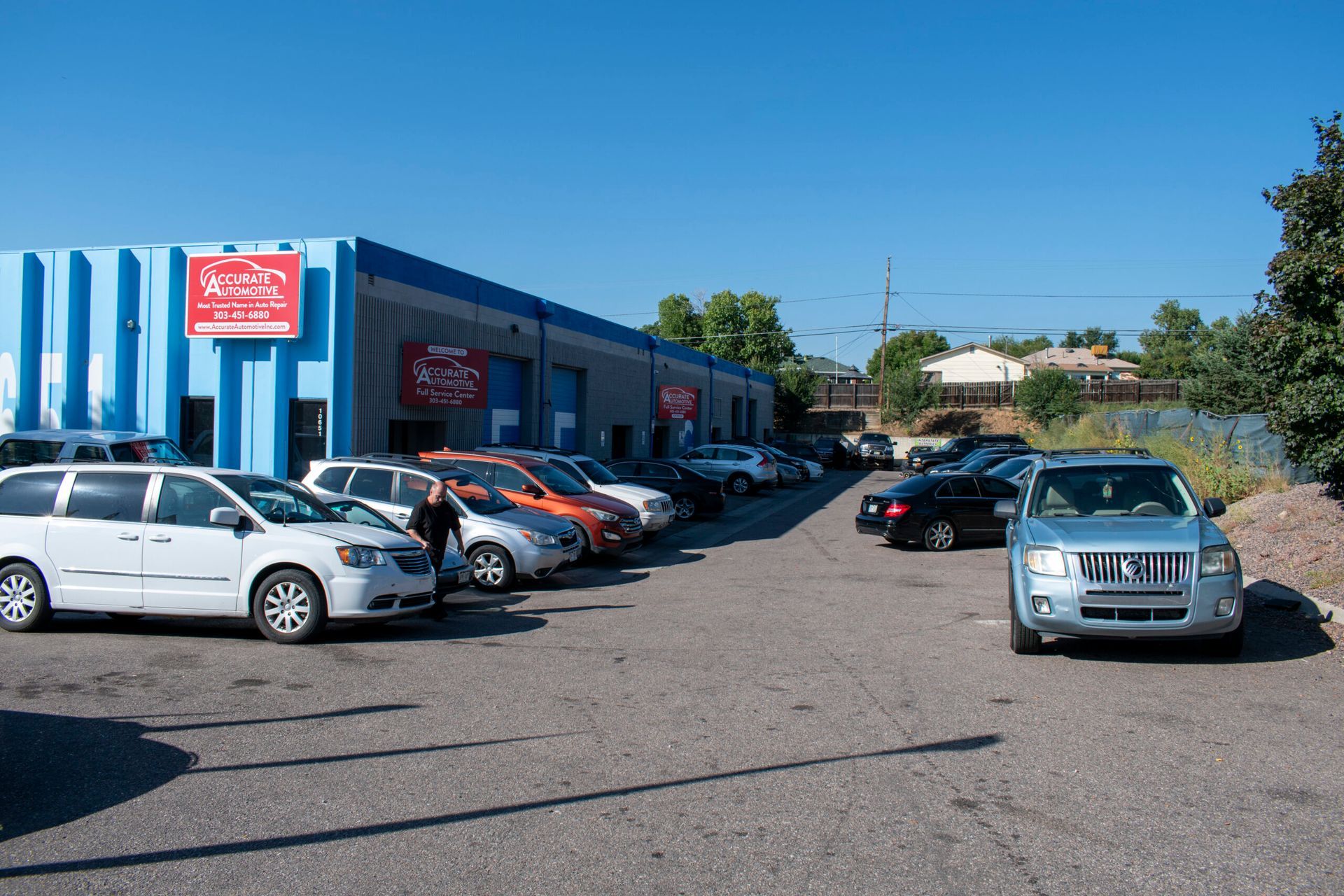 Parking lot outside a blue storefront with rows of parked cars on a sunny day | Accurate Automotive Northglenn