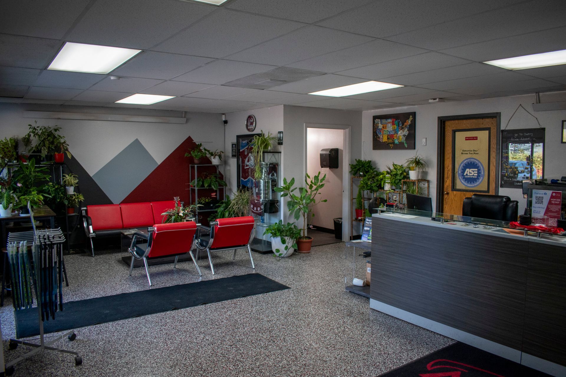 Modern office lobby with red chairs, plants, front desk, and wall art | Accurate Automotive Northglenn