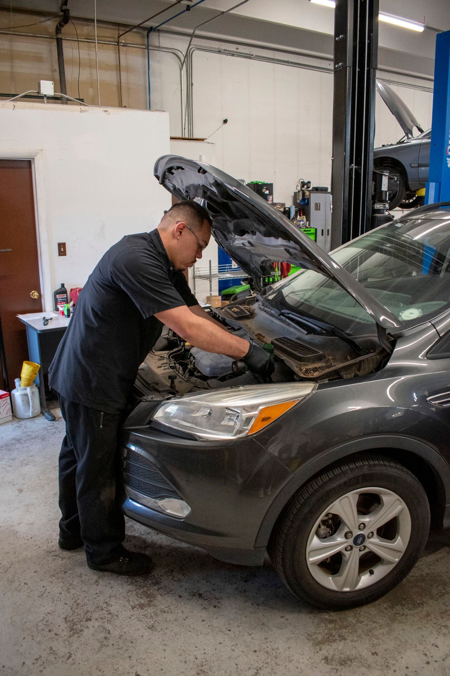 Mechanic working under the hood of a gray car in an auto repair shop | Accurate Automotive Northglenn