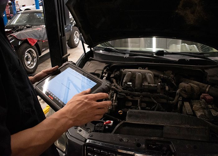 Mechanic using a tablet to diagnose a car engine with the hood open in a garage | Accurate Automotive Northglenn