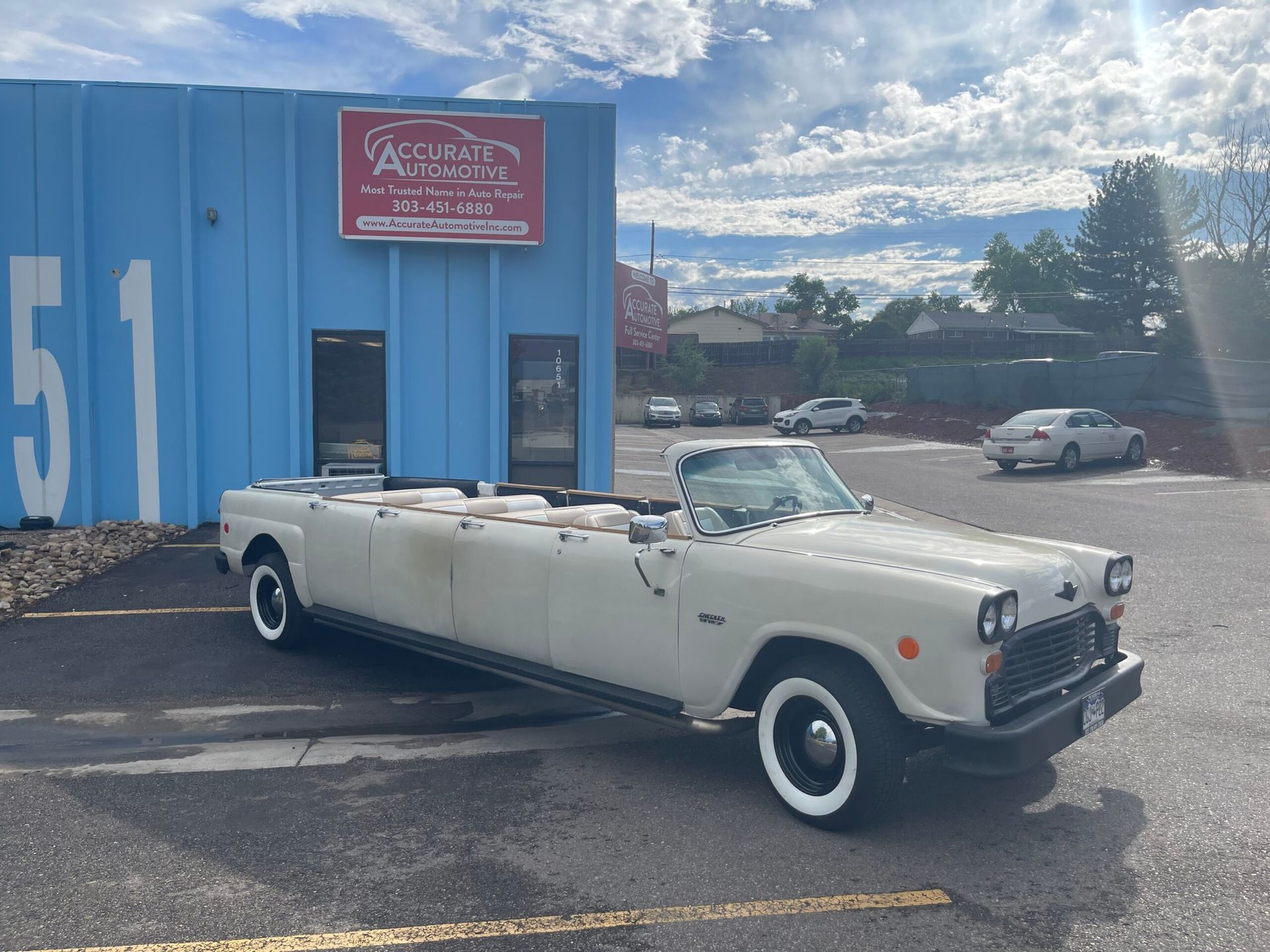 White vintage convertible parked outside a blue building under a cloudy sky. | Accurate Automotive Northglenn