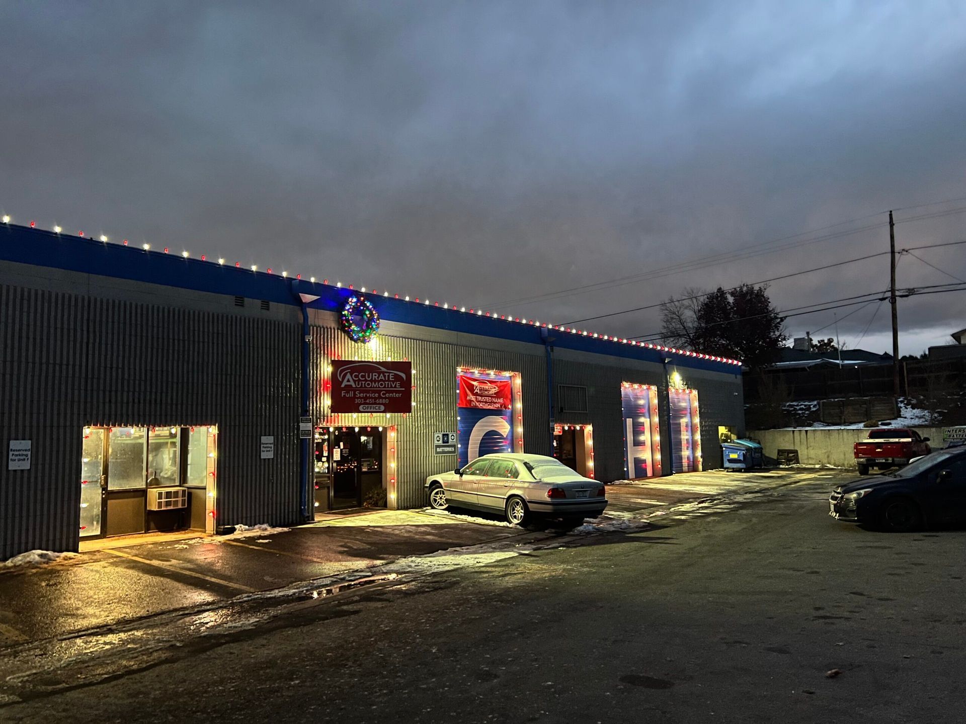 Snowy parking lot outside a lit convenience store at dusk, with parked cars and wet pavement. | Accurate Automotive Northglenn